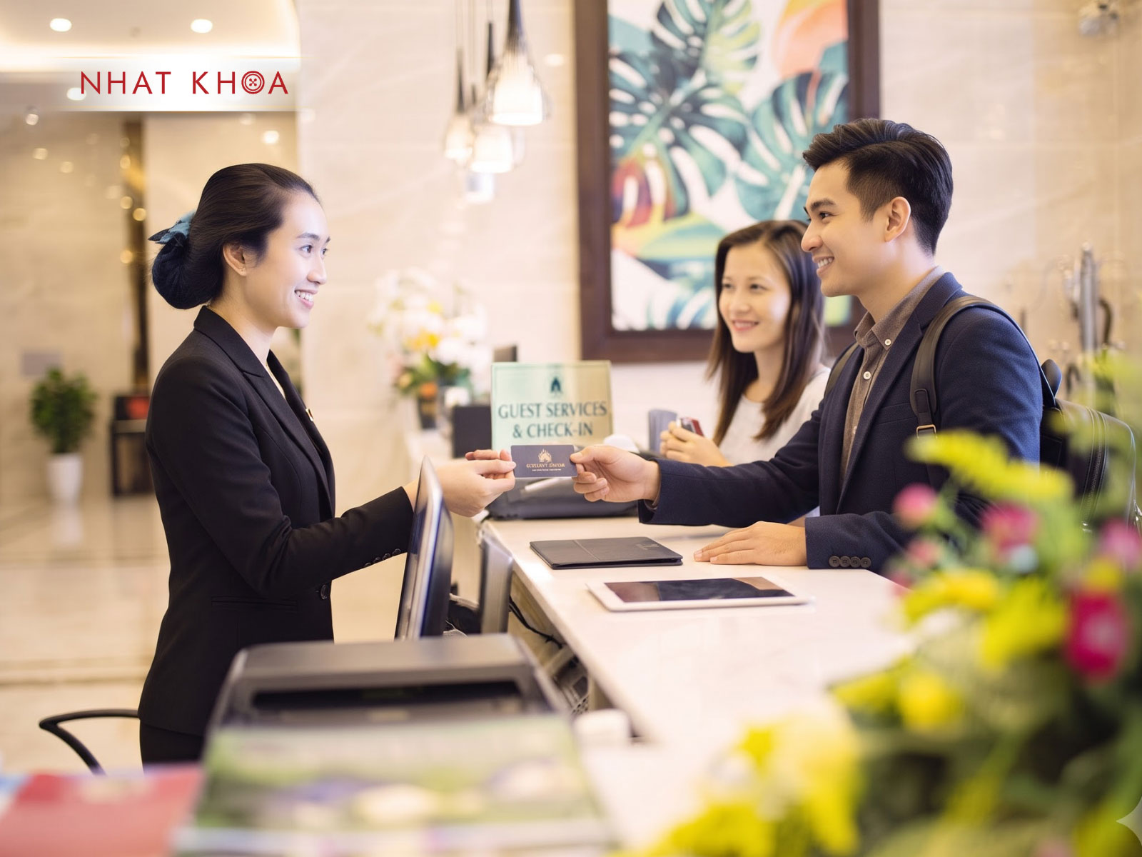 Đồng phục lễ tân nữ vest đen chuyên nghiệp tại quầy tiếp đón khách sạn.